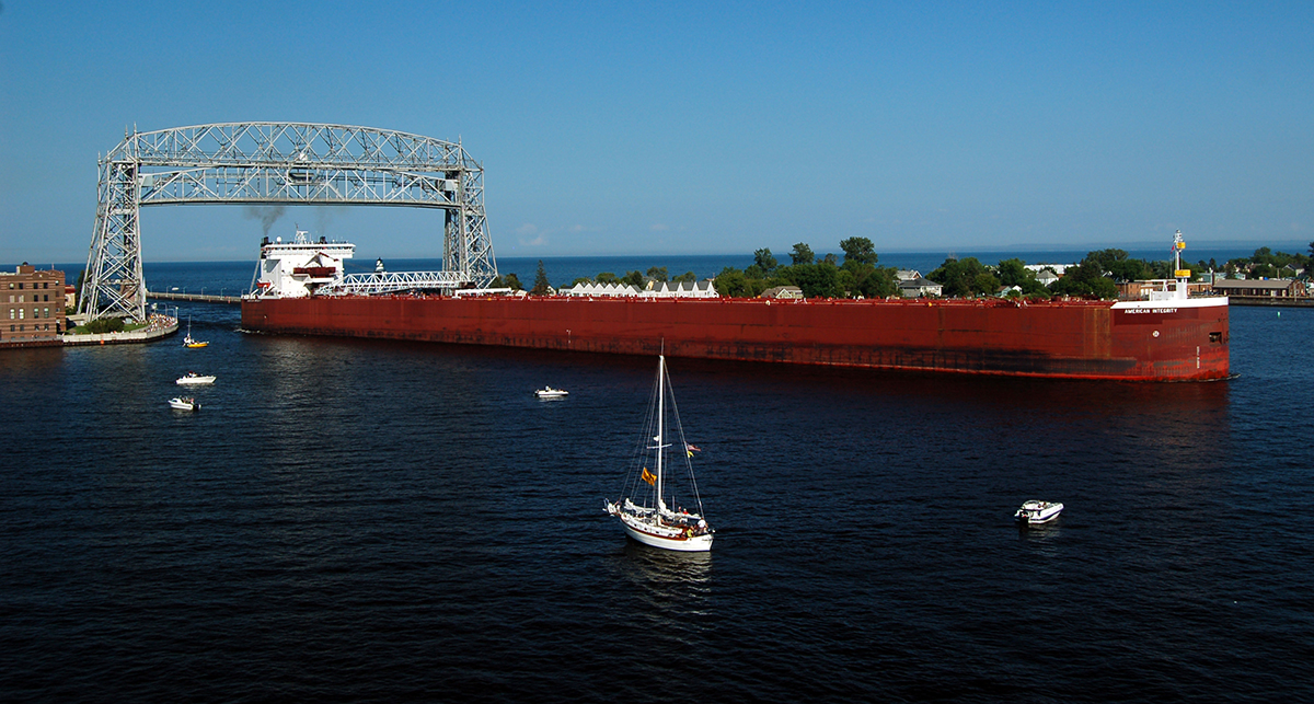 Large red ore ship sailing below aerial lift bridge