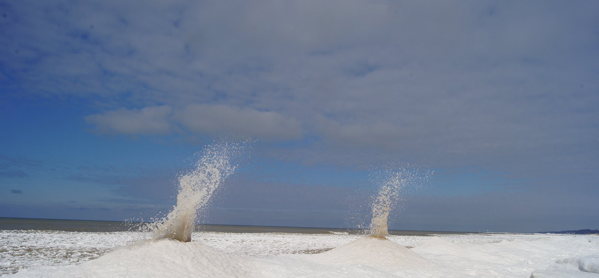 Two ice formations called volcanoes erupting water on shore of Lake Michigan.