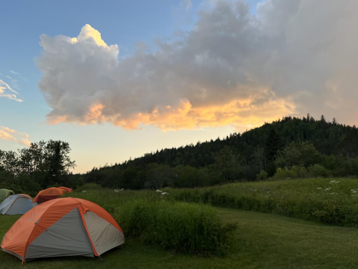 Tent on grass, hill in background, clouds in sky.