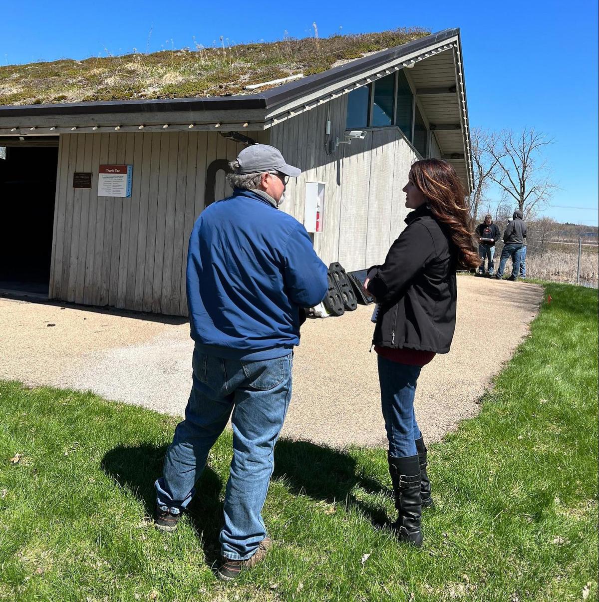 Two people standing by a building with a roof covered in vegetation.