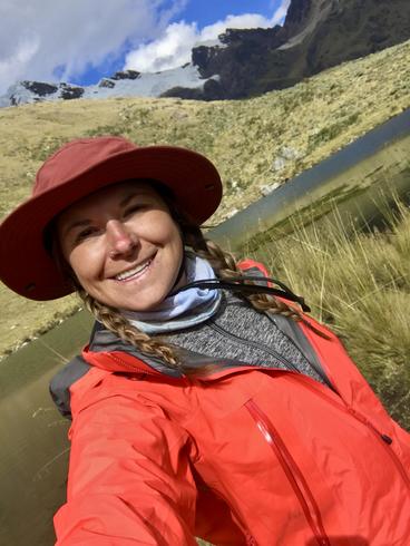 Tamera Breidenbach smiles in front of a Peruvian grassland and mountains.